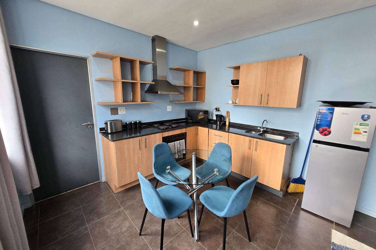 A functional kitchen featuring light wood cabinetry, dark granite countertops, a stainless steel extractor fan, and a built-in oven with a hob.
