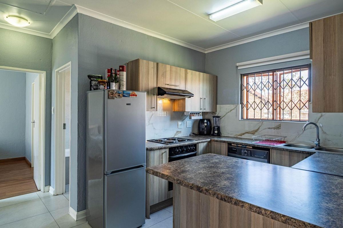 Functional kitchen featuring wood-look cabinetry, stone-effect laminate countertops, built-in hob and extractor fan, and a stainless steel sink with tiled splashback.