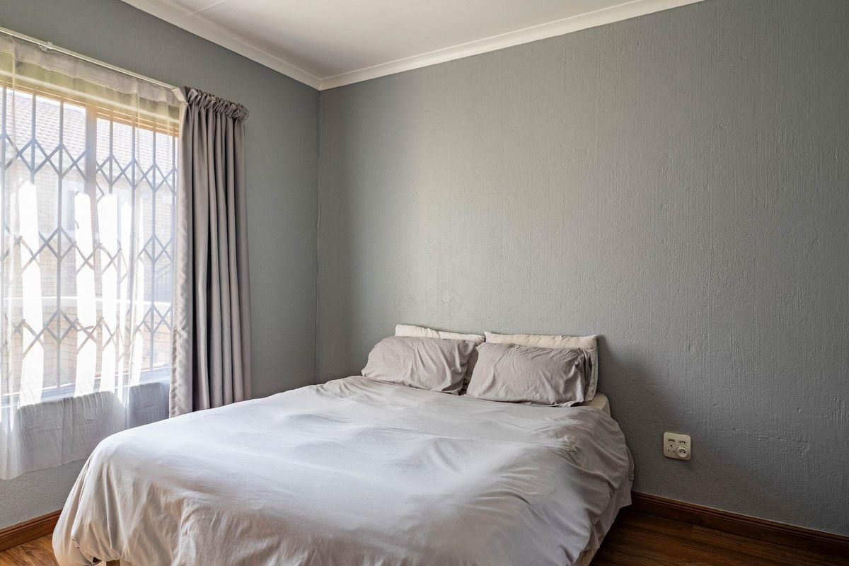 A bedroom featuring laminate flooring, a window with security bars, and neutral grey painted walls.