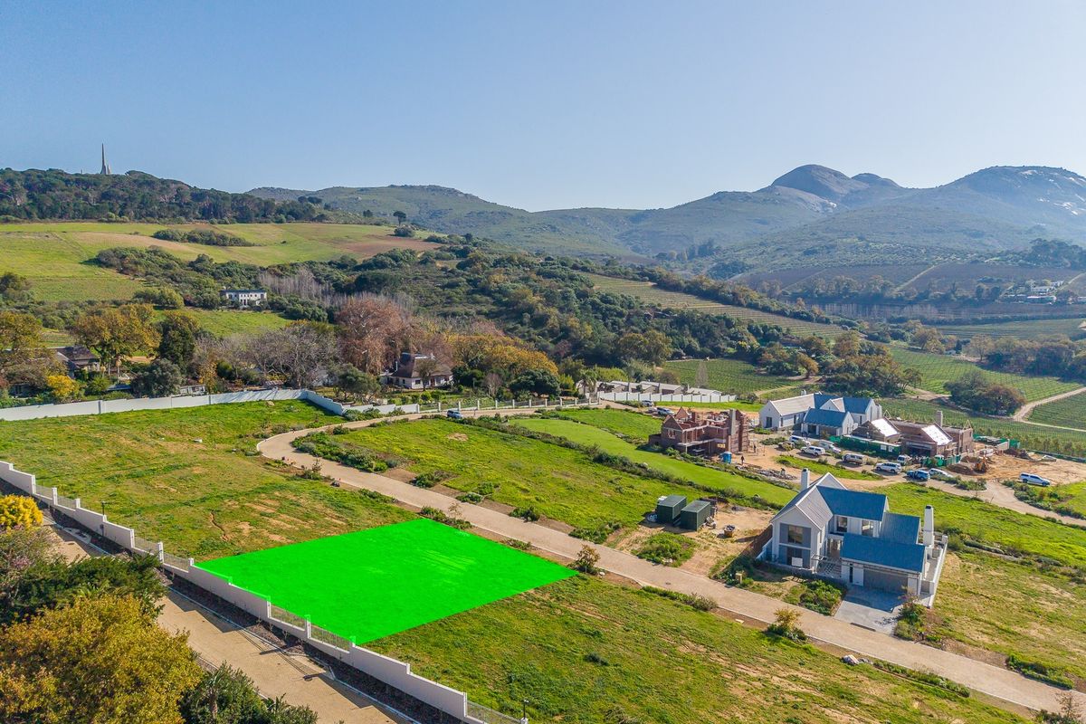An aerial view of a vacant residential plot highlighted in green, situated within a scenic estate with surrounding mountain and landscape views.