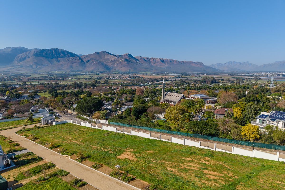 Aerial view of a vacant residential plot featuring established boundary walls, overlooking a scenic town with mountain vistas.