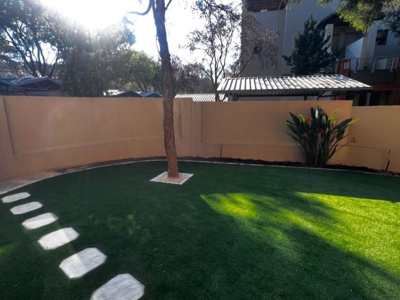 A well-maintained private garden area featuring artificial turf, stone stepping stones, and a perimeter boundary wall.