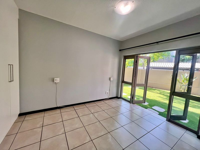 A bright, empty bedroom featuring tiled flooring, a built-in wardrobe, and direct access to a private garden through double glass doors.