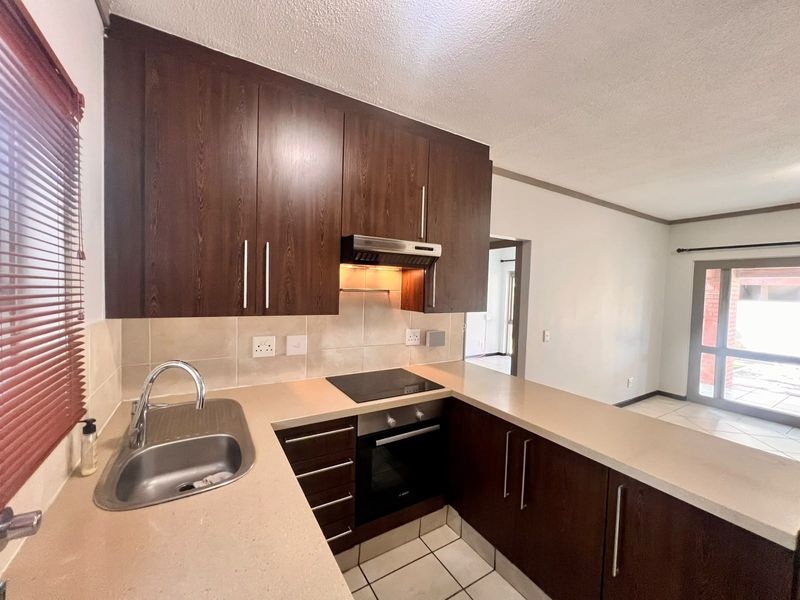 A functional kitchen featuring dark wood cabinetry, stone countertops, built-in oven, electric hob, and tiled flooring, offering a clean and well-maintained workspace.