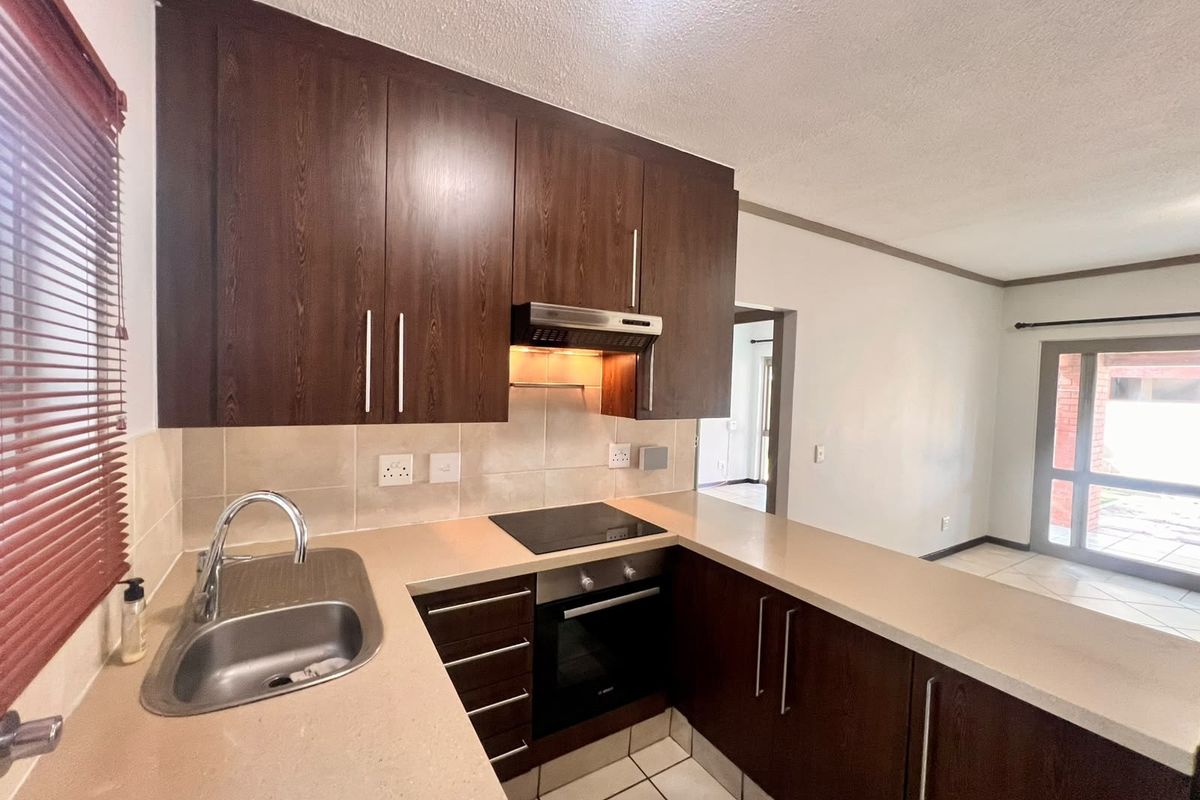 A functional kitchen featuring dark wood cabinetry, stone countertops, built-in oven, electric hob, and tiled flooring, offering a clean and well-maintained workspace.
