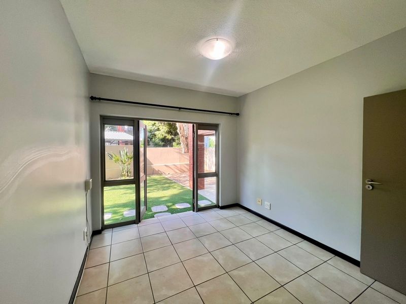 An empty bedroom featuring tiled flooring and a double glass door providing direct access to the garden area.