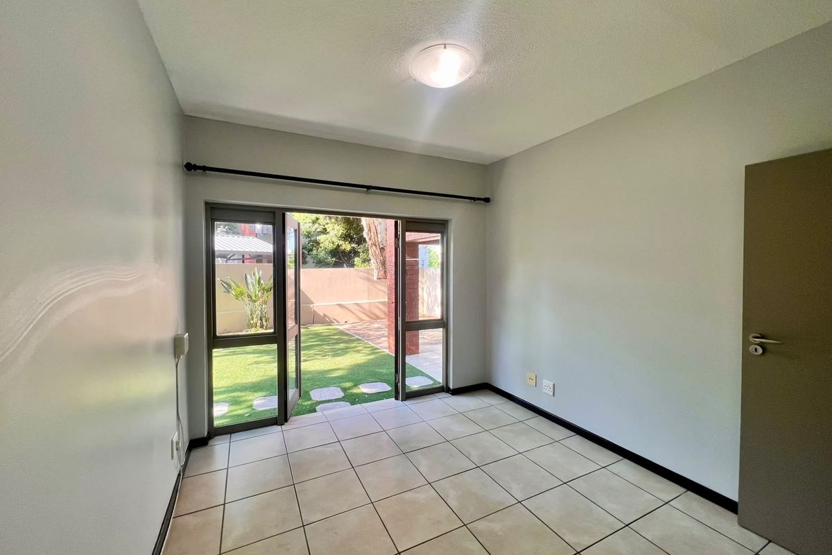 An empty bedroom featuring tiled flooring and a double glass door providing direct access to the garden area.