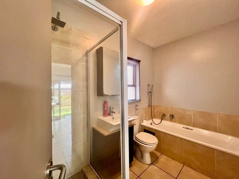 A functional bathroom featuring a separate shower enclosure, bathtub, built-in vanity with basin, and tiled finishes throughout.