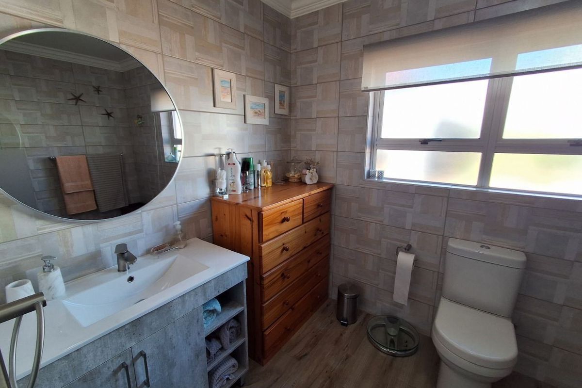 A well-maintained bathroom featuring modern wall tiling, a vanity with integrated basin, a toilet, and a window with a roller blind.