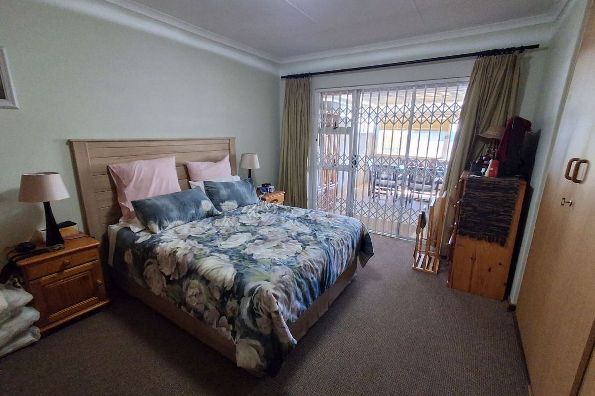 Spacious bedroom featuring built-in cupboards, carpeted flooring, and sliding glass doors with security gate providing direct access to the patio.