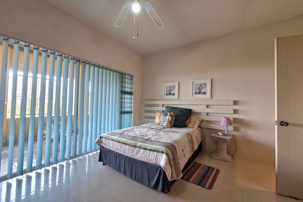 A spacious bedroom featuring large floor-to-ceiling windows with vertical blinds, tiled flooring, and a ceiling fan.