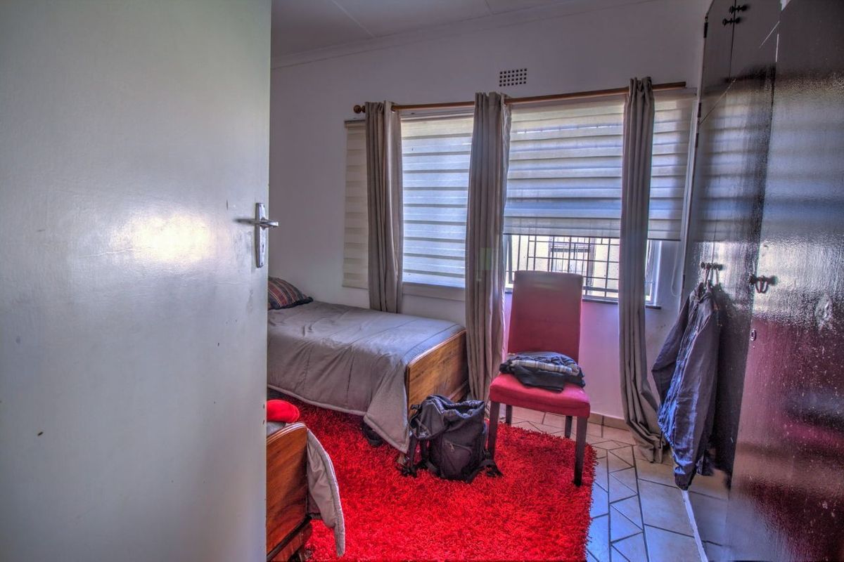 A compact bedroom featuring tiled flooring, built-in cupboards, and window treatments, offering a functional space with natural light.
