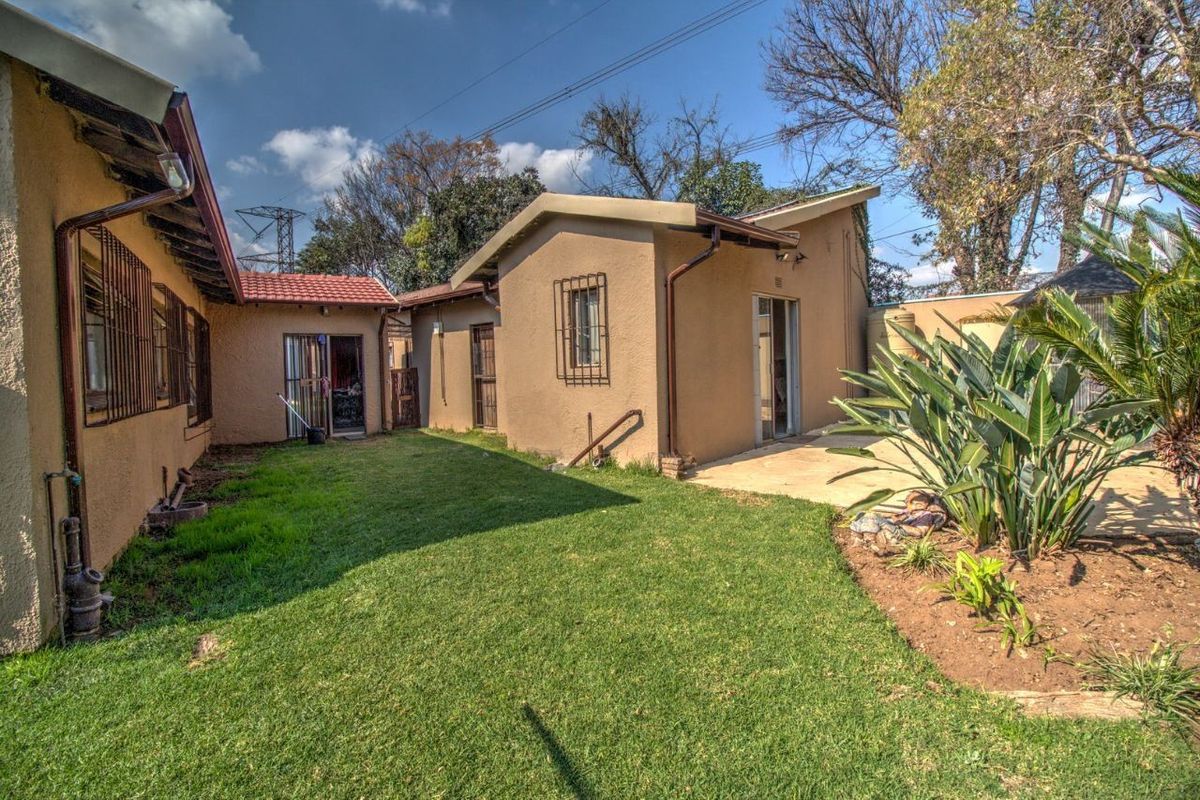 A view of the rear exterior of the house featuring a small lawn, paved patio area, and established garden beds.
