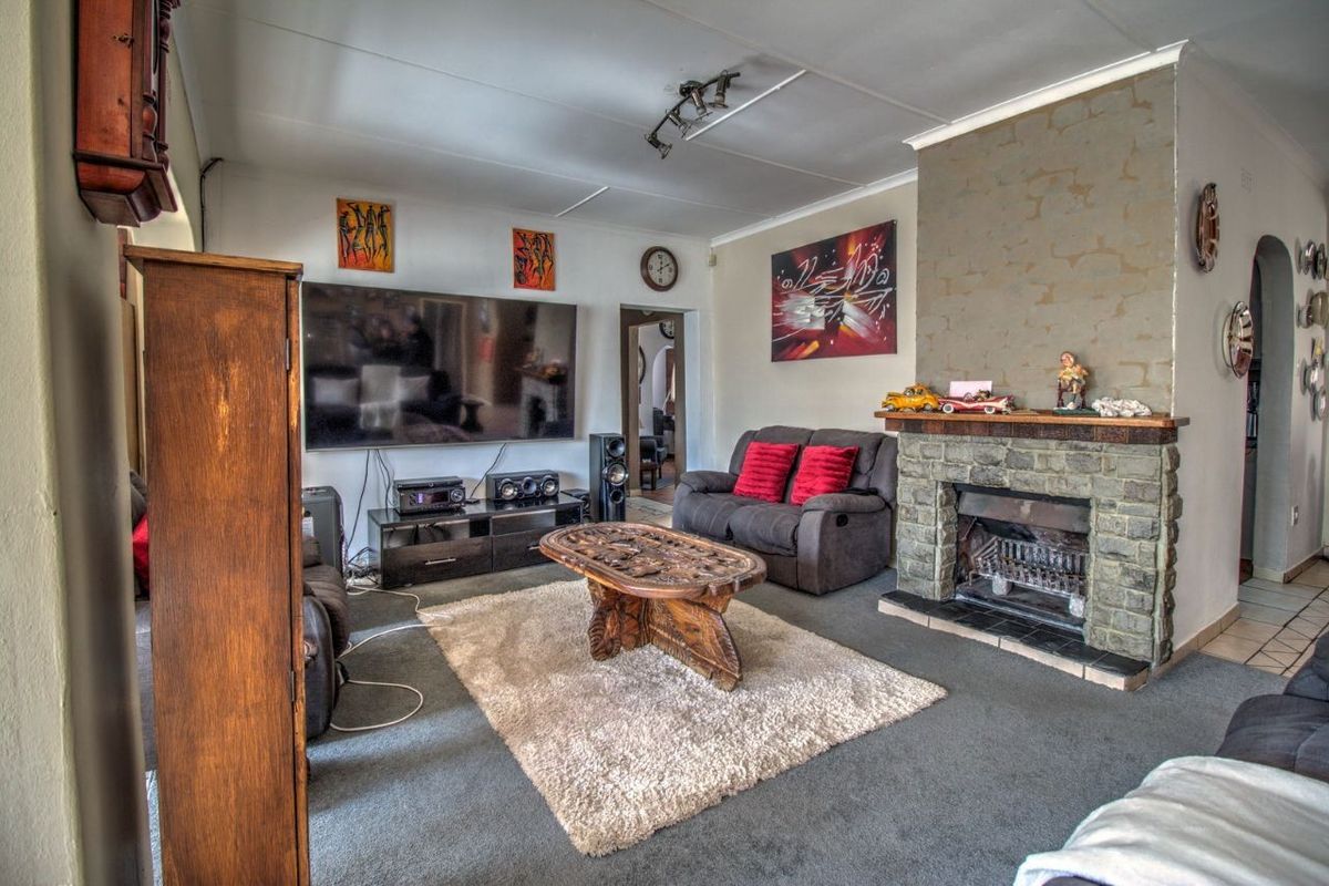 A living room featuring a stone-clad fireplace, carpeted flooring, and a ceiling-mounted track lighting system.