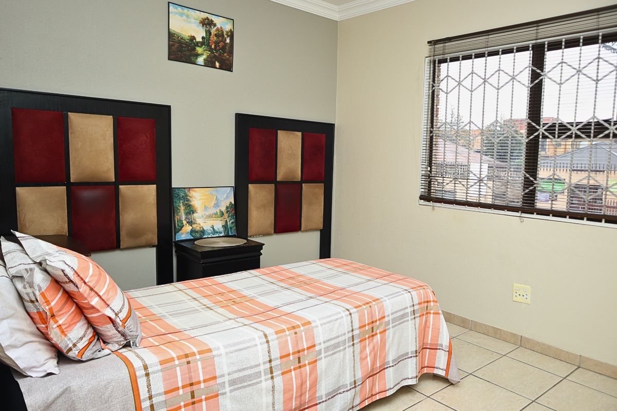 A functional bedroom featuring tiled flooring, a window with security bars, and built-in headboard panels.