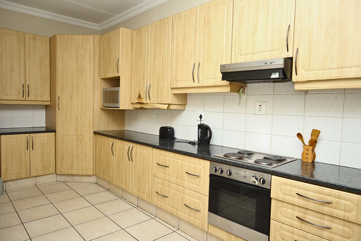 Functional kitchen featuring light wood-finish cabinetry, dark granite countertops, tiled flooring, and integrated stainless steel oven with extractor fan.