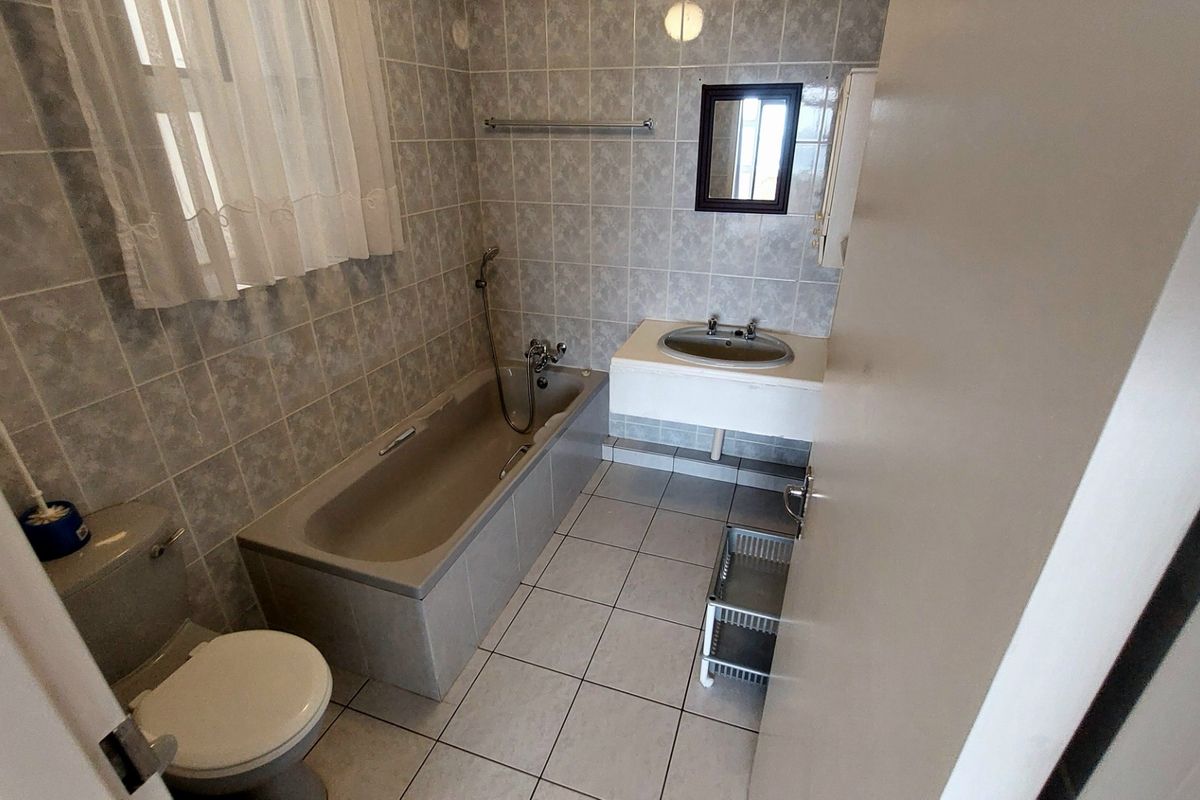 A dated bathroom featuring a built-in bathtub, wall-mounted vanity basin, and full-height wall tiling.