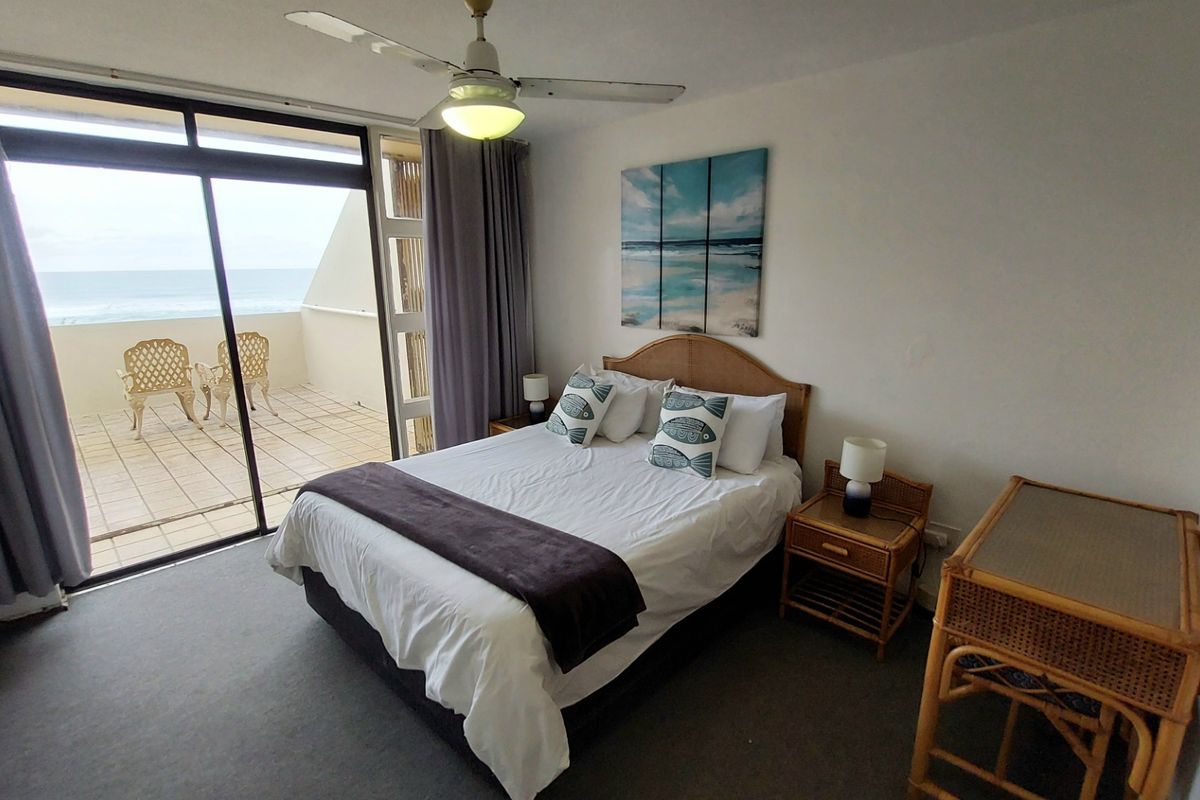 A bedroom featuring a ceiling fan and large sliding glass doors that open onto a private balcony with ocean views.