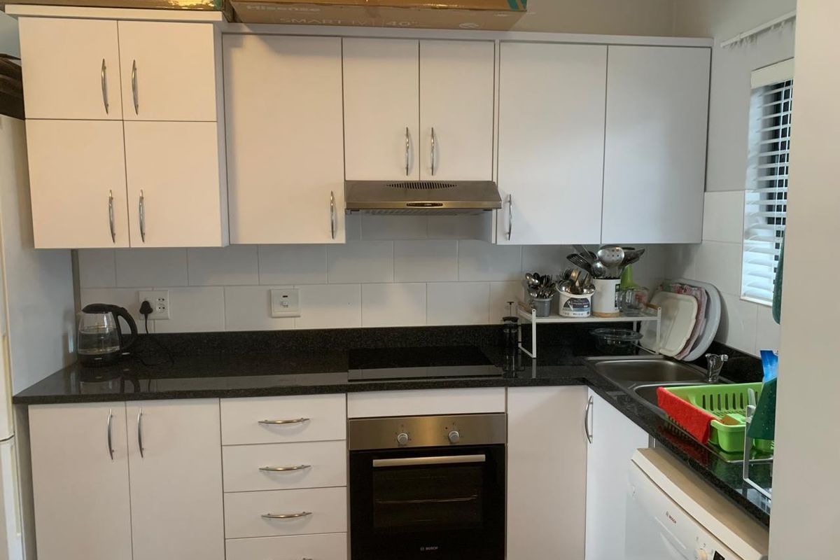 A functional kitchen featuring white cabinetry, dark granite countertops, a built-in oven, electric hob, and stainless steel extractor fan.