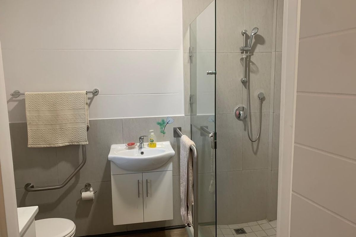 A modern, accessible bathroom featuring a walk-in glass shower, wall-mounted vanity basin, toilet, and safety grab rails for added convenience.