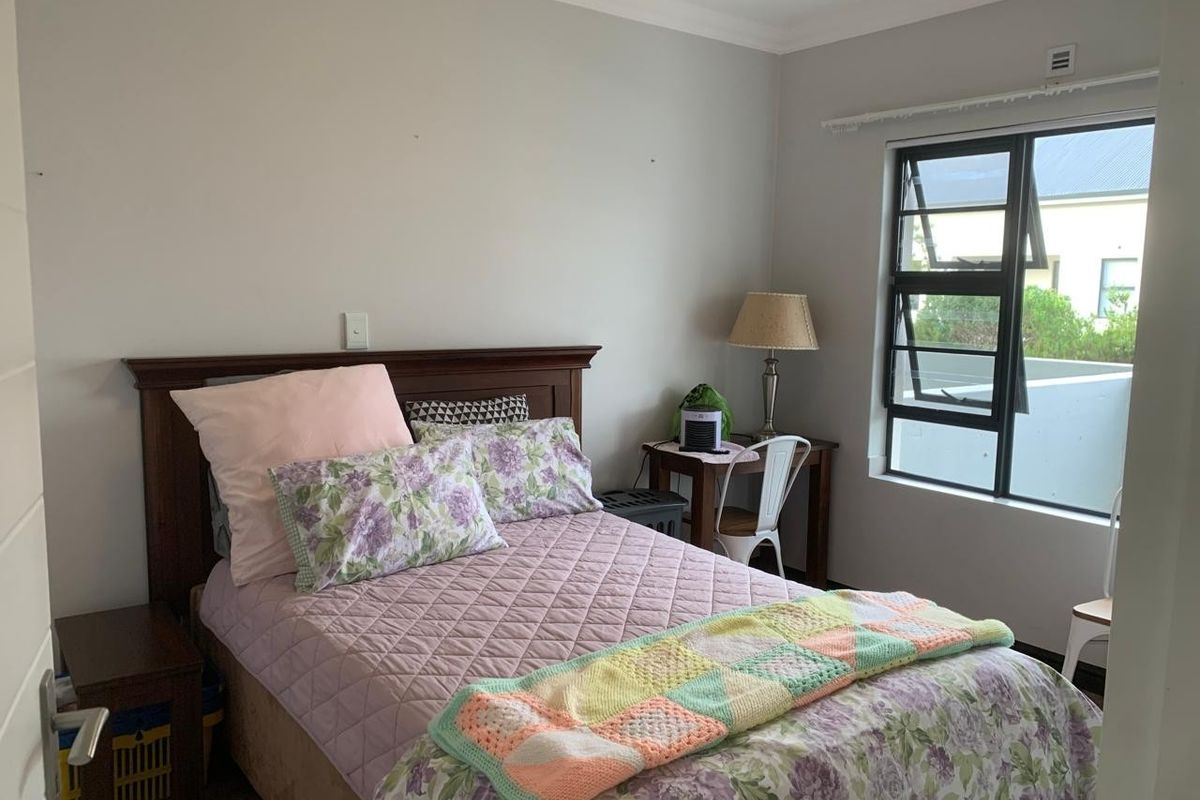 A well-lit bedroom featuring neutral walls, a large window with dark frames, and crown molding, providing a comfortable and functional living space.