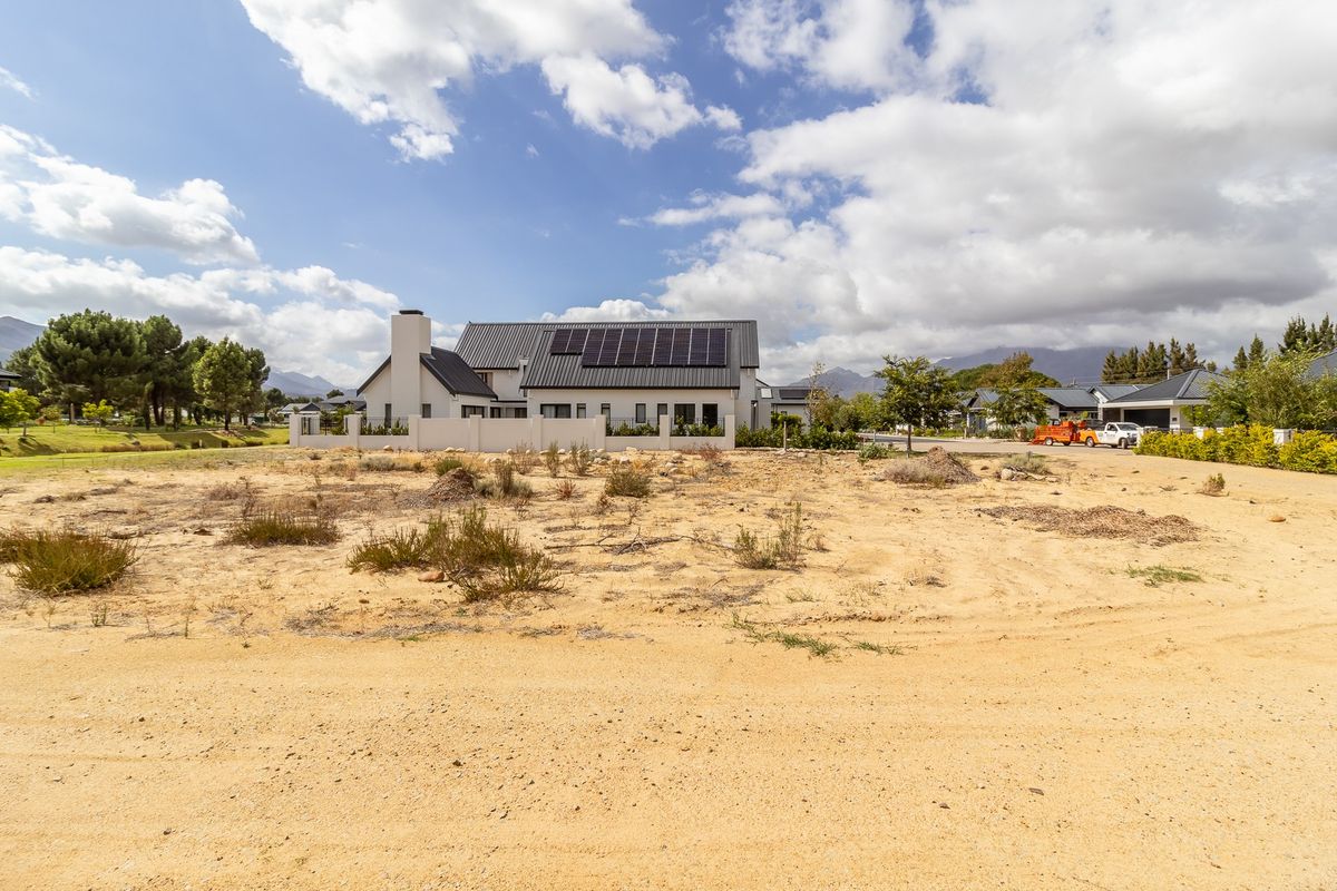 A vacant residential plot of land with a view of a neighboring modern house featuring a metal roof and solar panels.