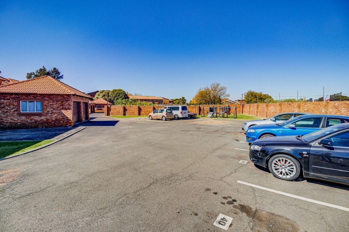 Exterior view of the apartment complex parking area featuring paved surfaces, brick boundary walls, and a small children's play area.