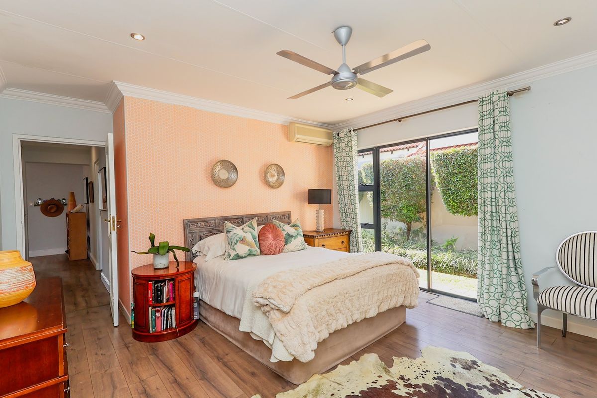 Spacious bedroom featuring laminate flooring, a ceiling fan, split-system air conditioning, and sliding glass doors providing direct access to the garden.