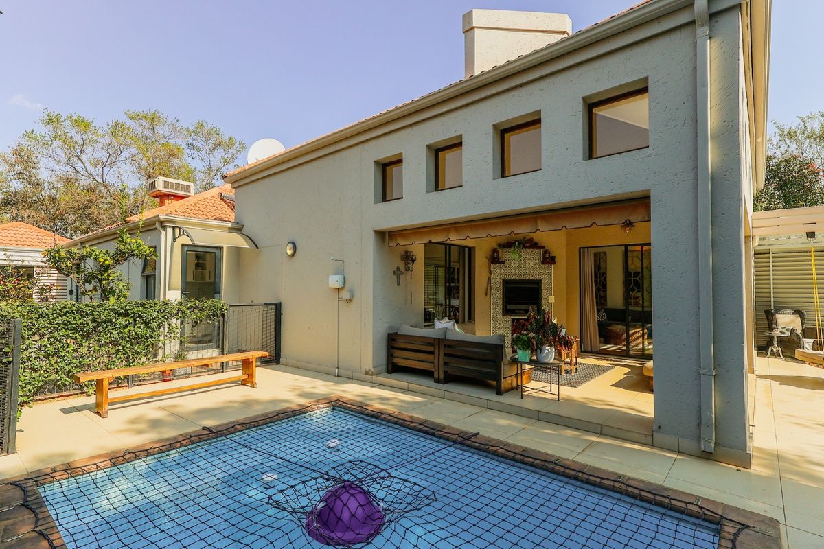 Rear exterior view featuring a covered patio with a built-in fireplace, tiled flooring, and a swimming pool with a safety net.