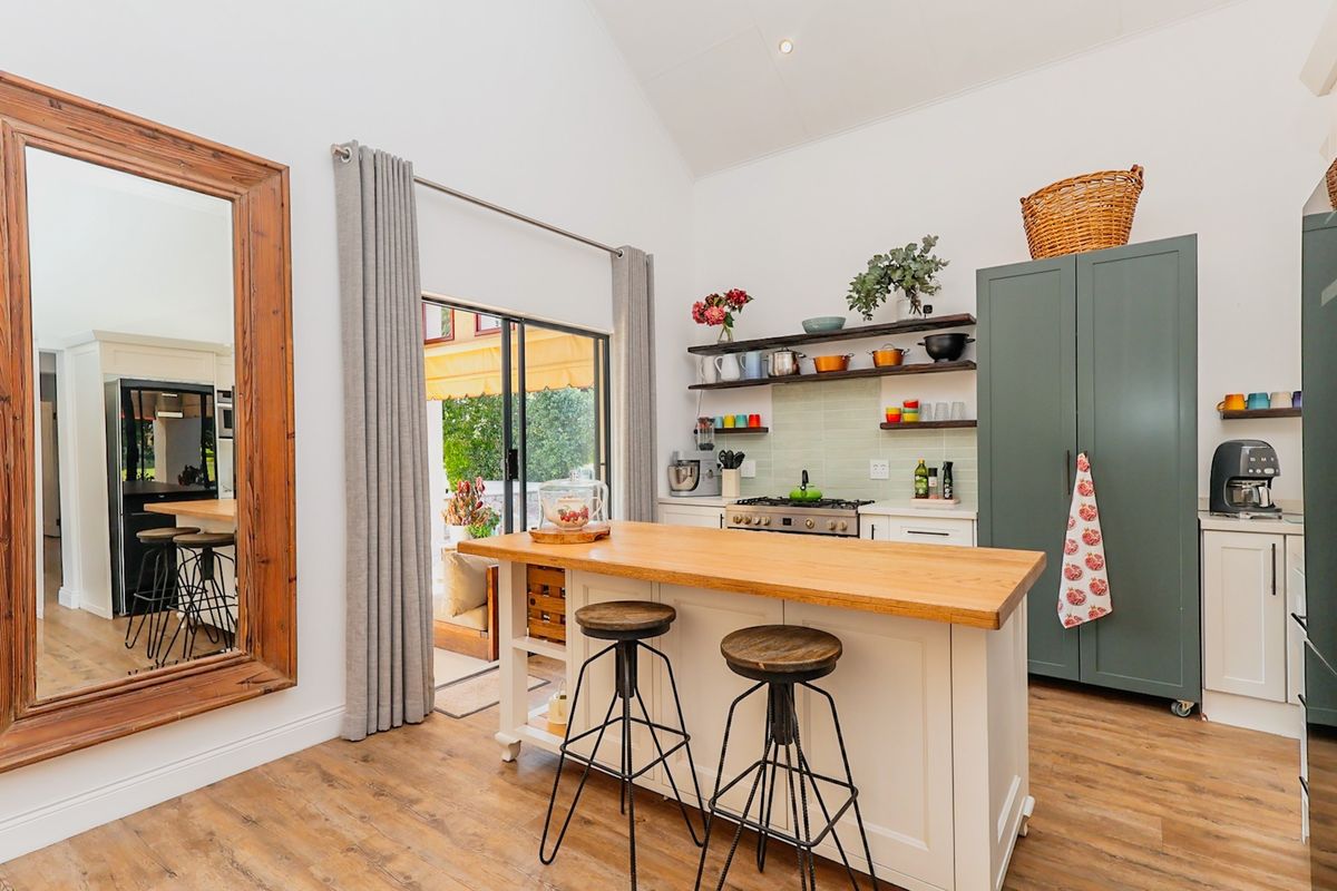 Modern kitchen featuring a central timber-topped island, gas hob, floating shelving, and direct access to the outdoor patio area through sliding glass doors.