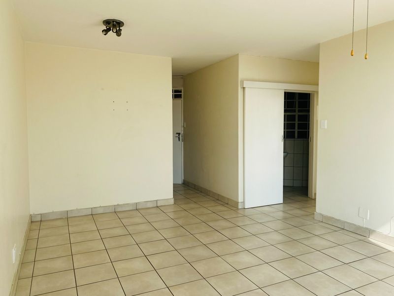 An empty, neutral-toned living area featuring ceramic floor tiles, a sliding door, and simple ceiling lighting, offering a blank canvas for personalization.