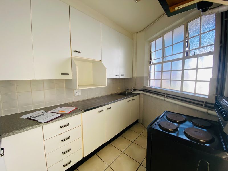 A functional kitchen featuring white built-in cabinetry, laminate countertops, a stainless steel sink, and tiled flooring with natural light from a steel-framed window.