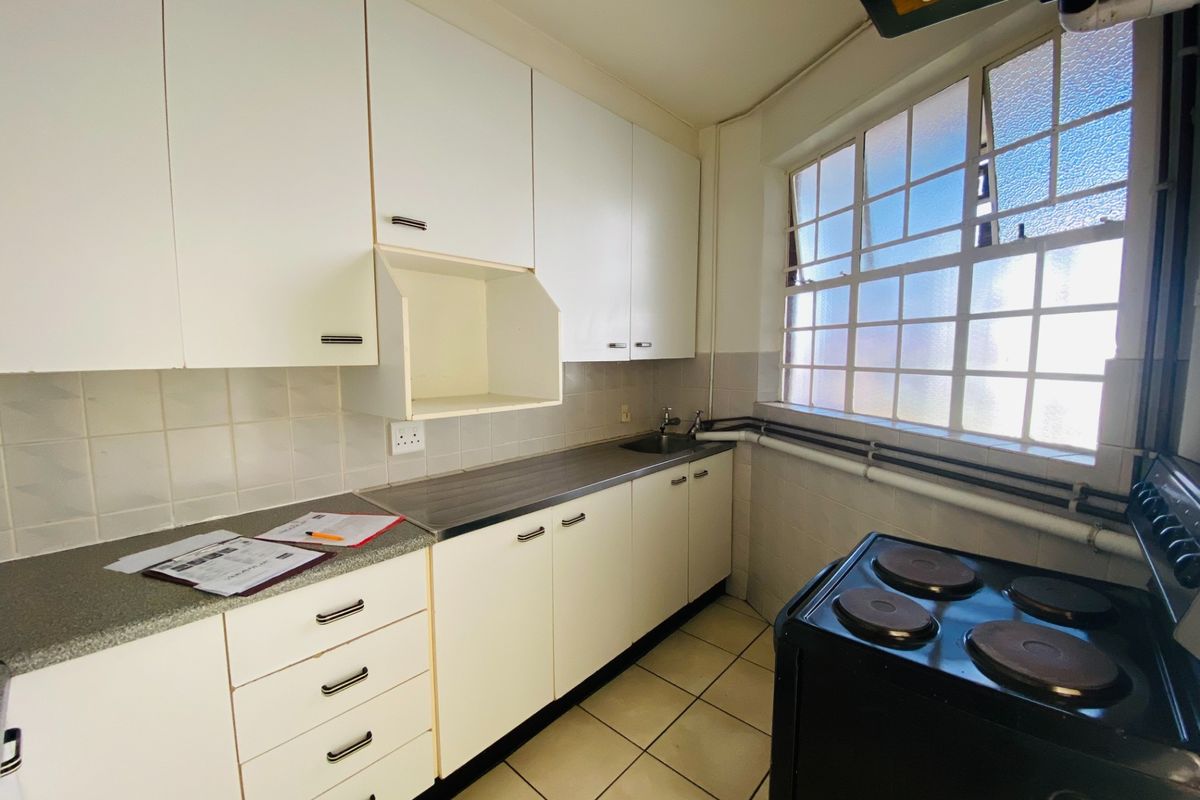 A functional kitchen featuring white built-in cabinetry, laminate countertops, a stainless steel sink, and tiled flooring with natural light from a steel-framed window.