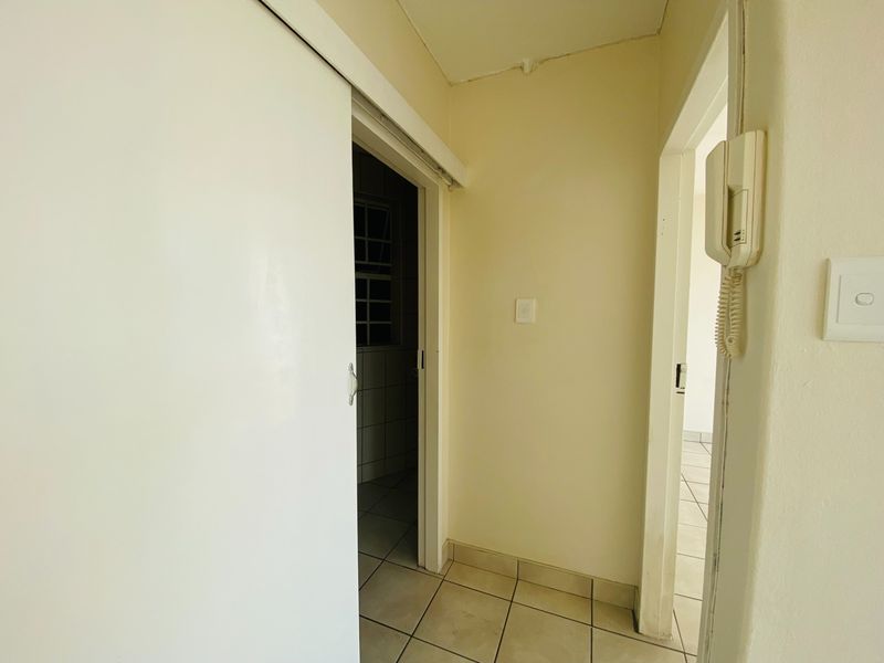 A functional hallway featuring tiled flooring, a sliding door, and a wall-mounted intercom system, providing access to adjacent rooms.
