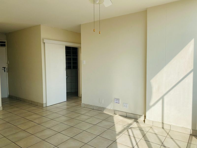 An empty living area featuring neutral ceramic floor tiles, a ceiling fan, and a sliding door leading to an adjacent room.