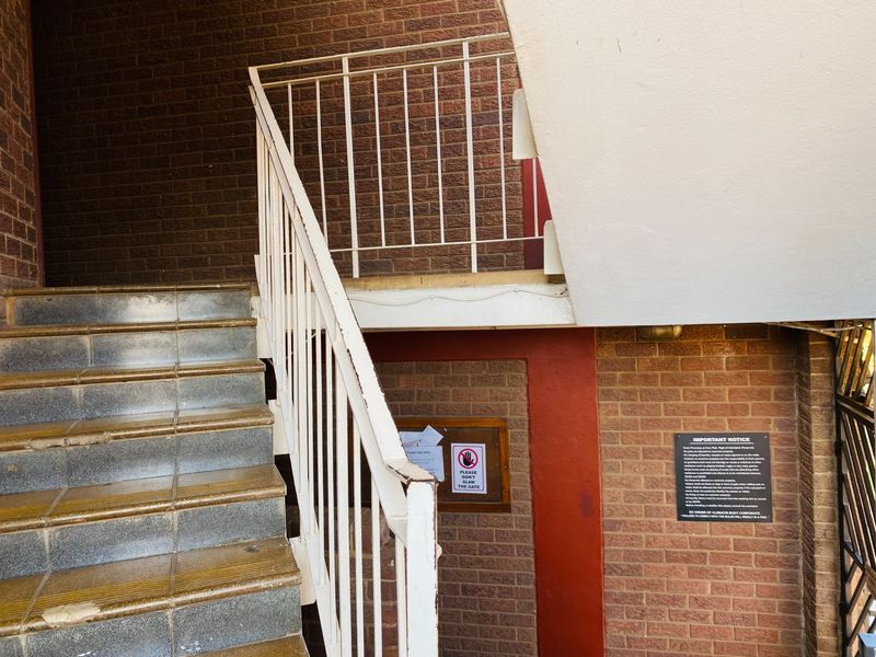 Exterior entrance area featuring a brick facade, metal staircase with tiled steps, and a communal notice board.