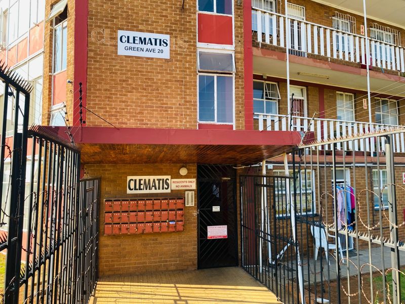 Front entrance view of Clematis apartment complex featuring brick facade, communal mailboxes, and security perimeter fencing.