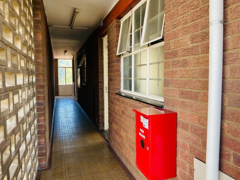 An exterior-facing apartment hallway featuring brick walls, a decorative breeze block screen, tiled flooring, and a wall-mounted fire hose reel.