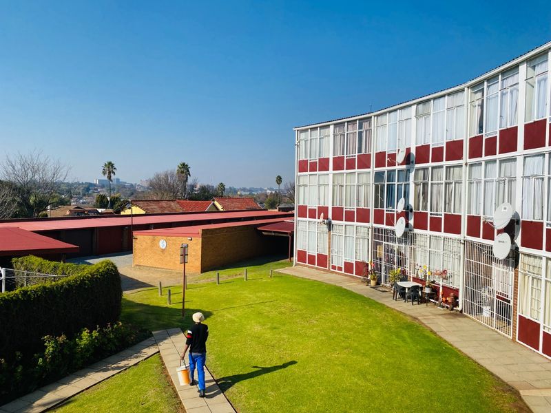 Exterior view of an apartment complex featuring a shared lawn, paved walkways, and brick garage structures under a clear sky.