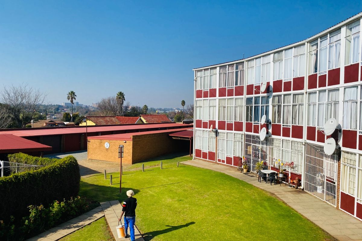 Exterior view of an apartment complex featuring a shared lawn, paved walkways, and brick garage structures under a clear sky.