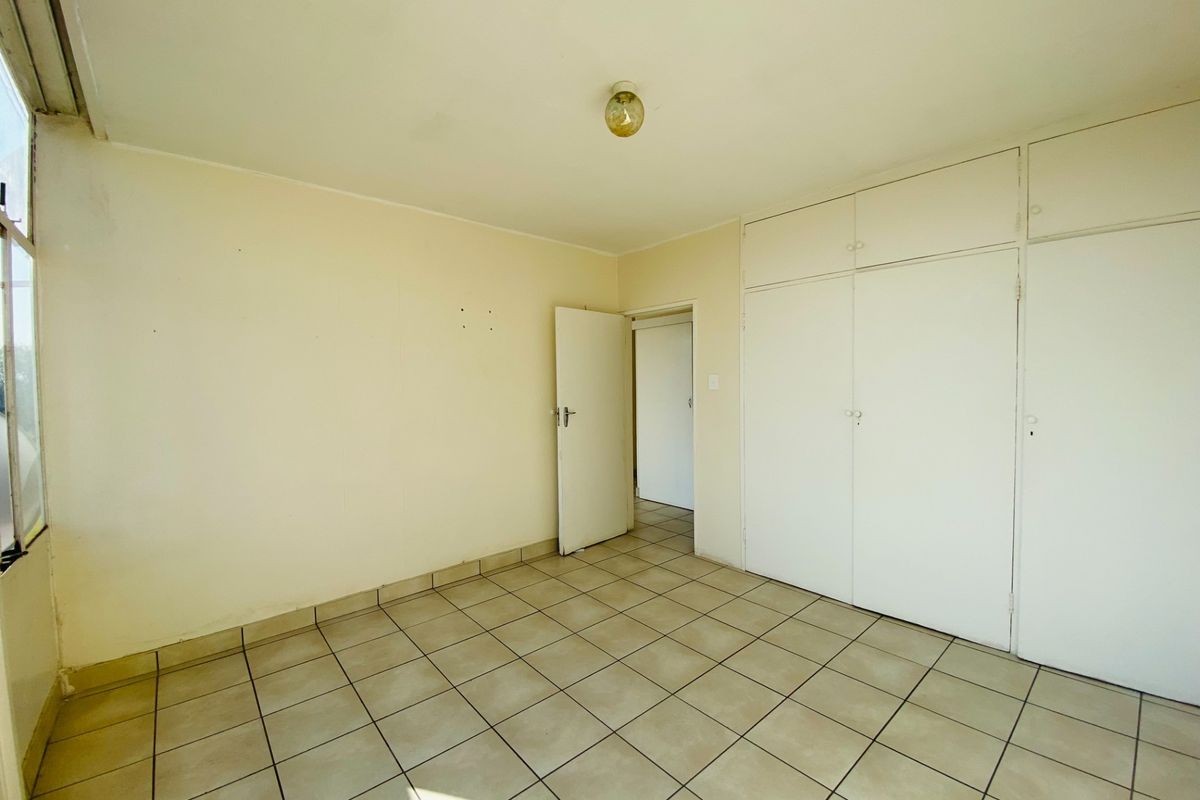 An empty bedroom featuring tiled flooring and built-in cupboards, offering a blank canvas for personalization.