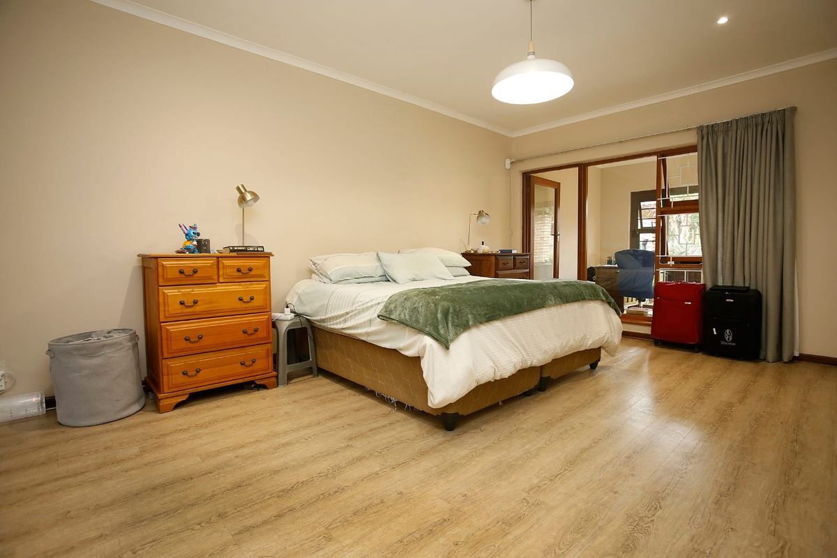 Spacious bedroom featuring light wood-look laminate flooring, neutral walls, and sliding glass doors providing access to an adjoining sunroom or patio area.