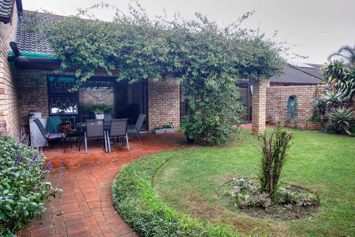A private rear garden featuring a paved patio area with a pergola, established lawn, and perimeter brick walling.