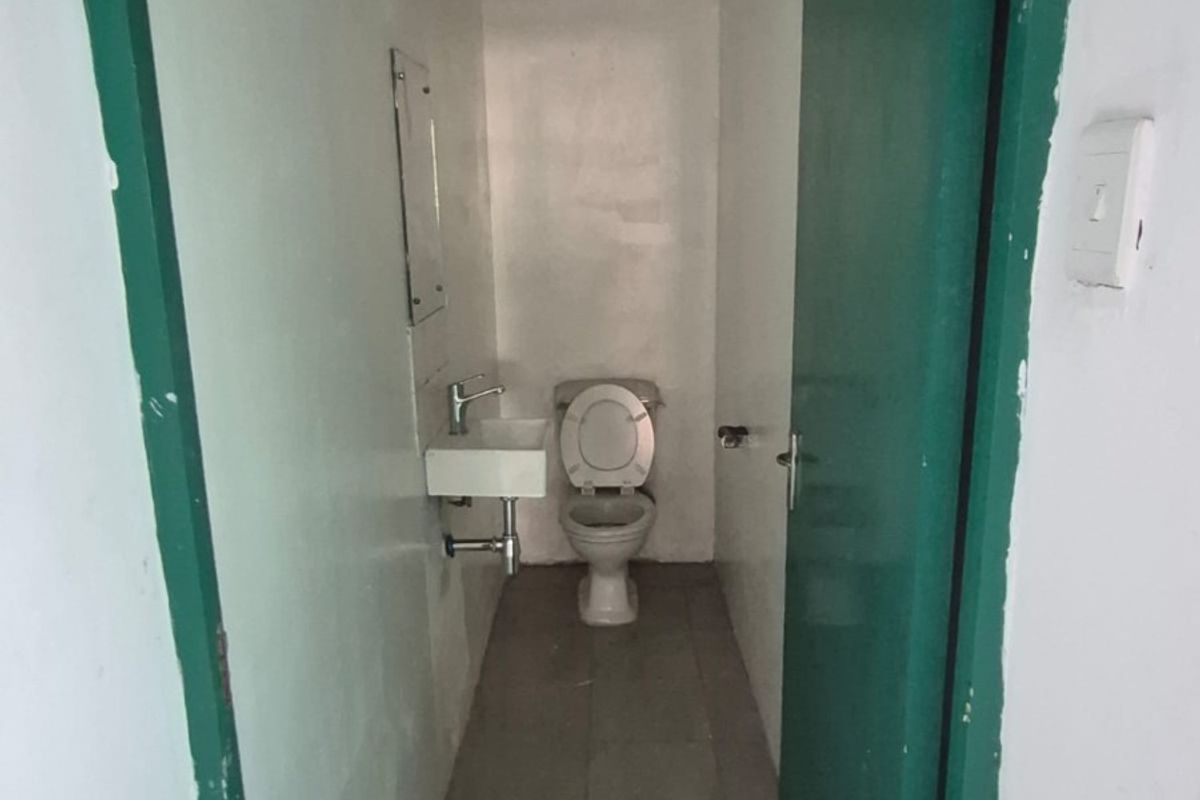A compact industrial-style restroom featuring a wall-mounted basin and toilet, finished with tiled flooring and painted door frames.