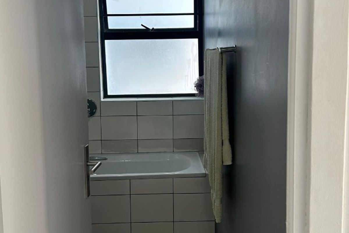 A compact bathroom featuring a built-in bathtub with tiled surround, a frosted glass window, and neutral wall finishes.