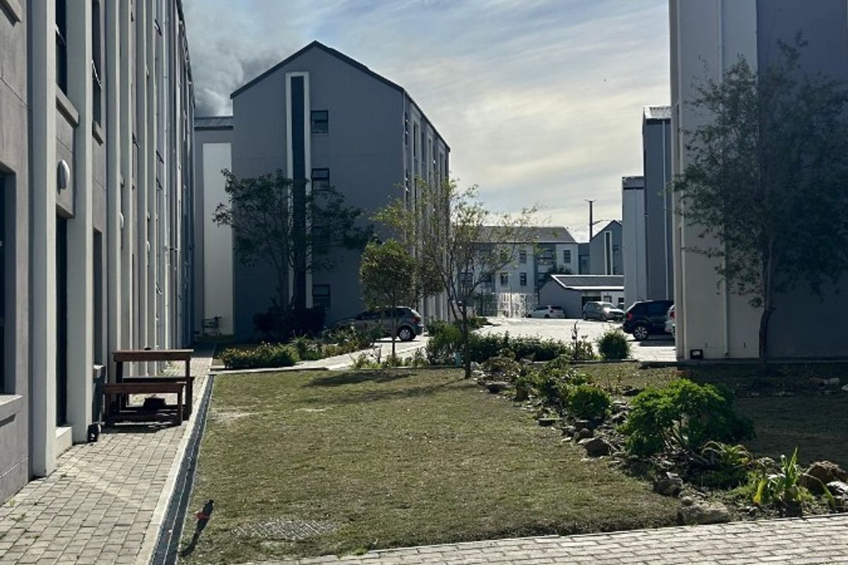 Exterior view of the apartment complex grounds featuring paved walkways, landscaped garden beds, and multi-story residential buildings.
