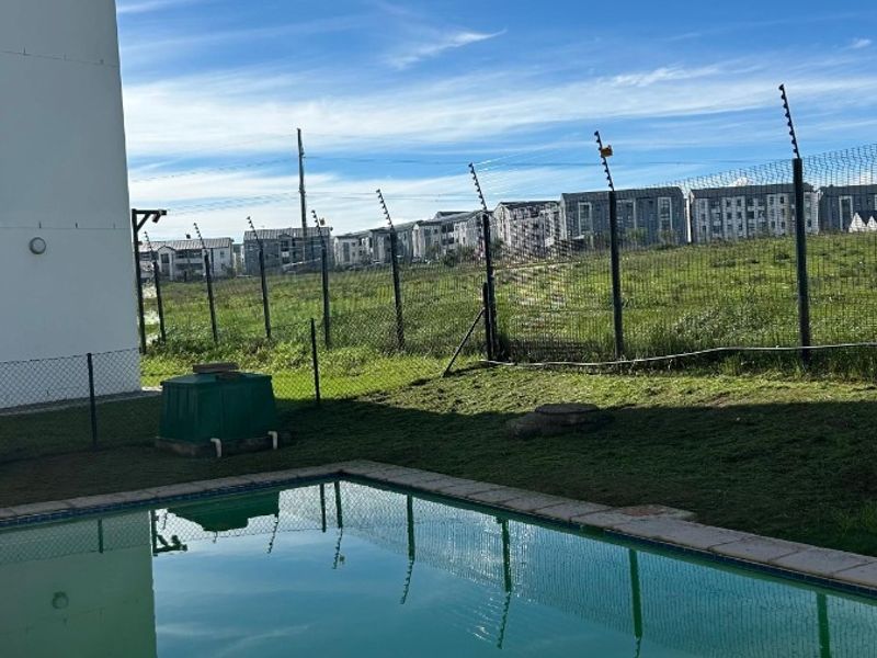 Outdoor pool area featuring a private swimming pool, perimeter fencing with security wire, and views of the surrounding residential complex.