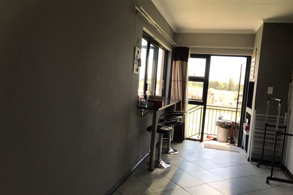 A bright living area featuring tiled flooring, a built-in breakfast bar, and direct access to a balcony through a glass door.