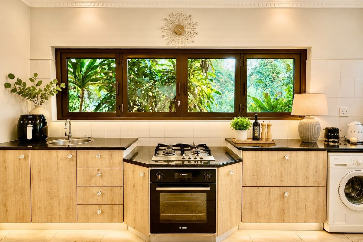 Modern kitchen featuring light wood cabinetry, black granite countertops, a built-in Bosch oven, gas hob, and integrated washing machine with garden views.