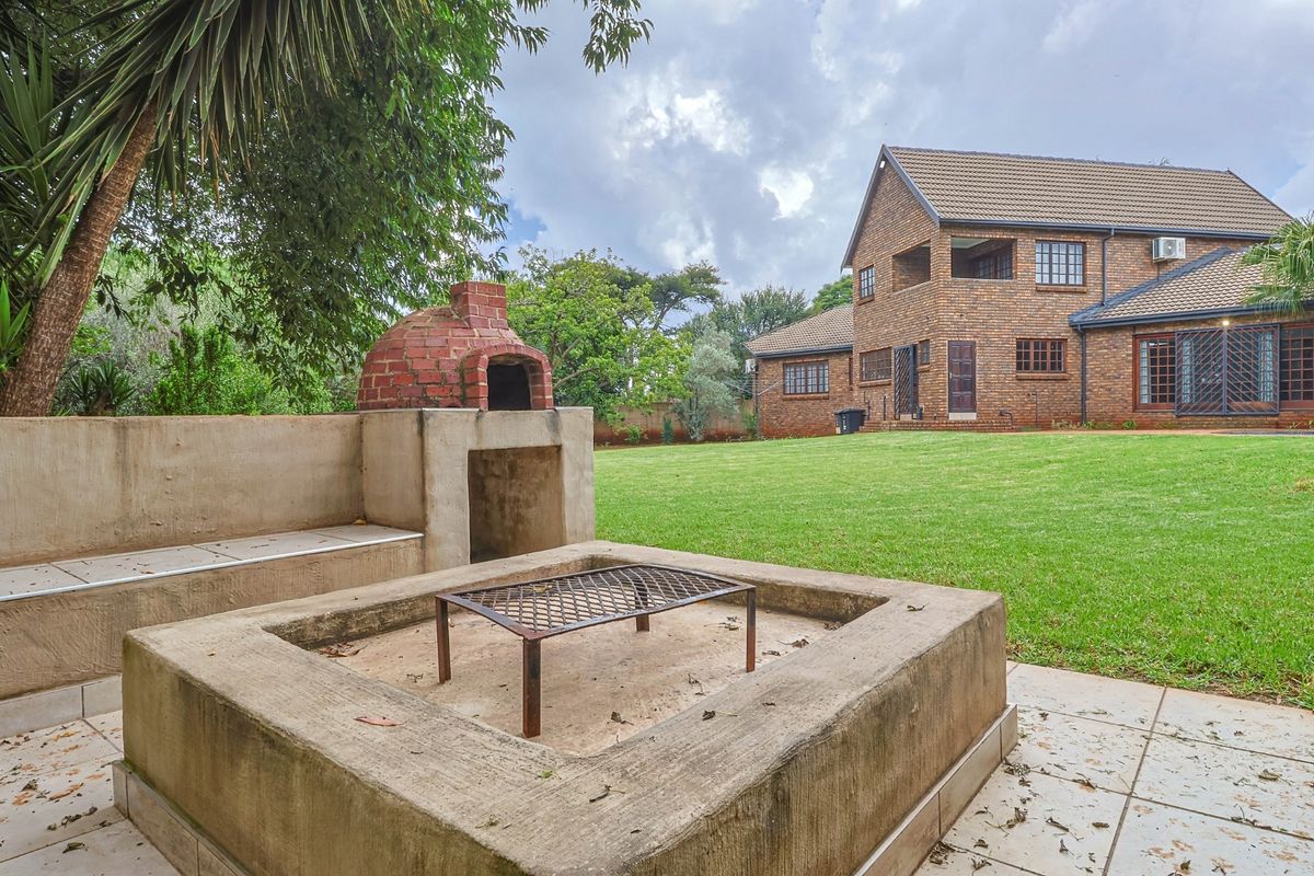 Spacious rear garden featuring a built-in brick pizza oven and a concrete fire pit area, set against a double-story face-brick house.